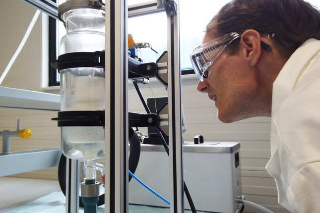 FlexxGroep engineer running a lab test on a glass reactor column with powder sorbent